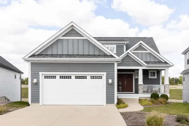 Grand Ledge, MI, USA - September 25, 2022: A new, grey home with horizontal and vertical siding, white garage door, and covered front porch.