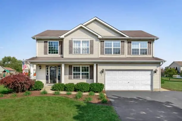 A new suburban house with tan siding, brown window shutters, and a front porch.