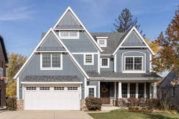 A blue and white modern farmhouse with a covered porch, grey roof, and two car garage.