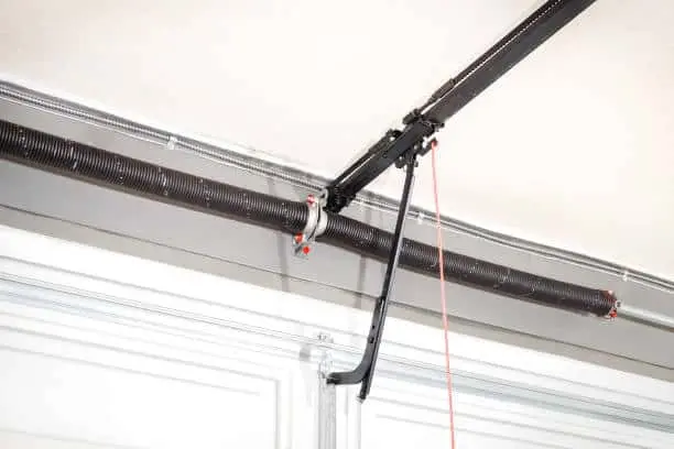 Close up of torsion spring, quick connect door arm, T-rail and chain. White garage door in home, parking facility or commercial gate. Selective focus.