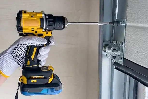 A garage door repair technician assembles sectional doors using a screwdriver. The concept of sectional door installation.