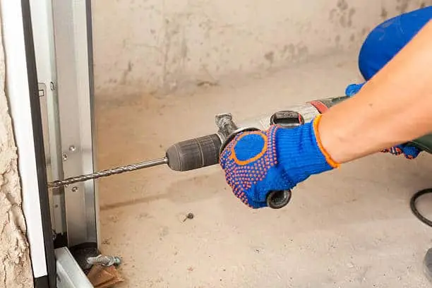 Garage doors installation. Worker drills a hole for the bolt.