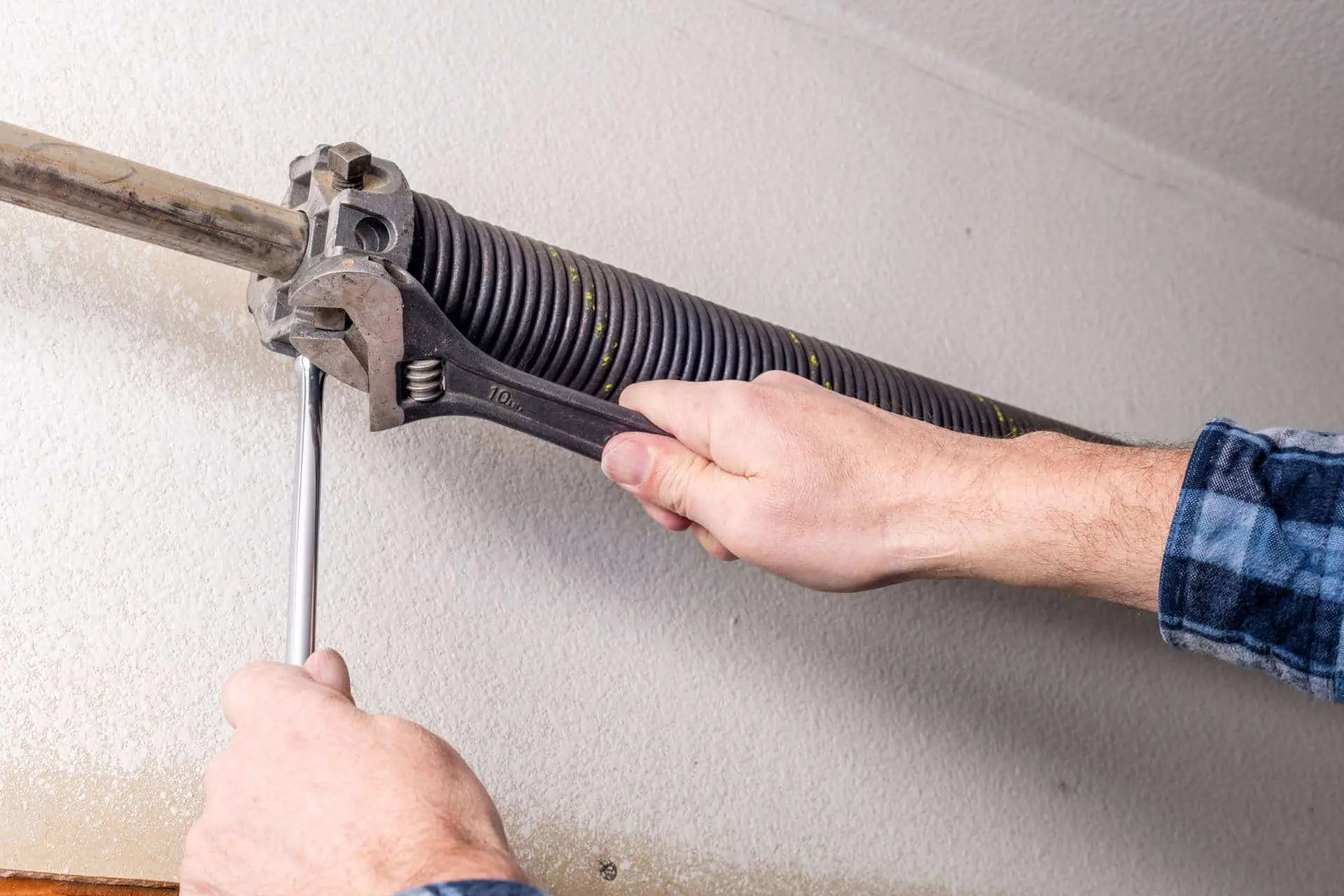 Two hands holding tools, fixing a garage door spring.