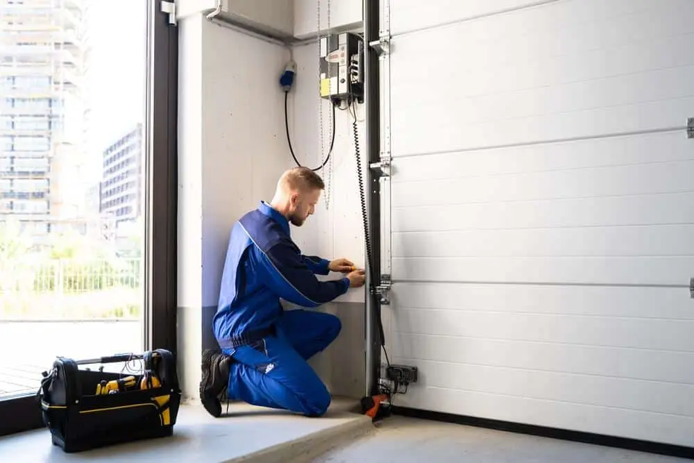A man kneeling while repairing a garage door.