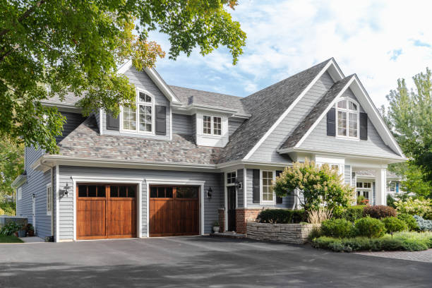 A large grey and white modern farmhouse with two wooden garage doors, and beautiful landscaping.