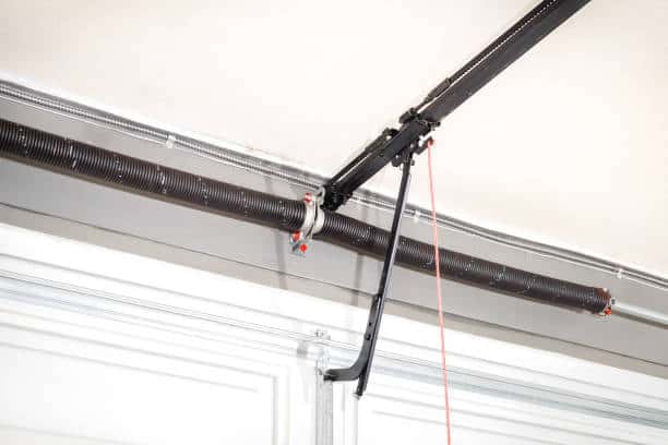 Close up of torsion spring, quick connect door arm, T-rail and chain. White garage door in home, parking facility or commercial gate. Selective focus.