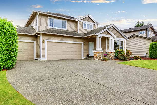 Neat beige home with two garage spaces and large concrete driveway.