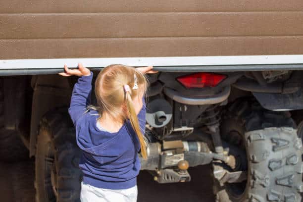 Little blond girl opening garage door where ATV stands.