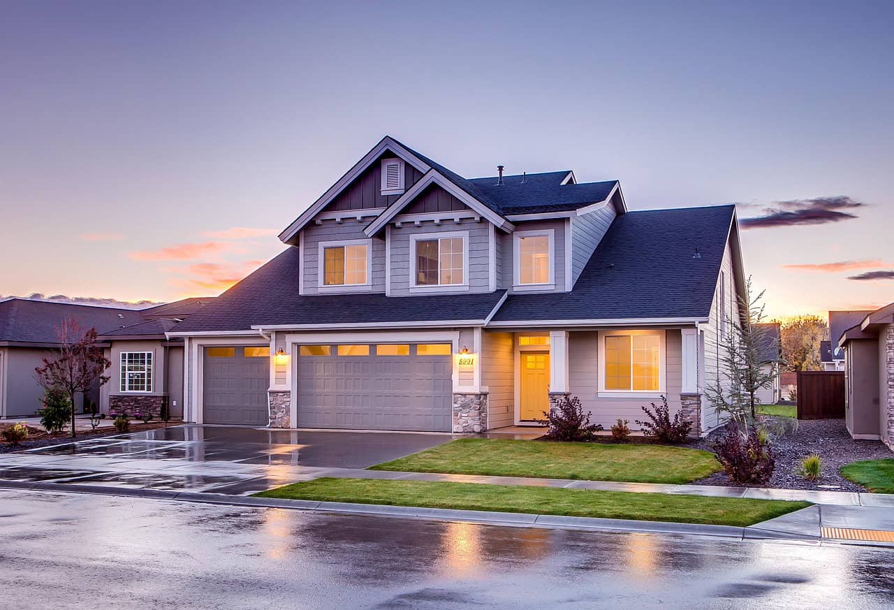 A modern house with wet driveway and sun set on the horizon.
