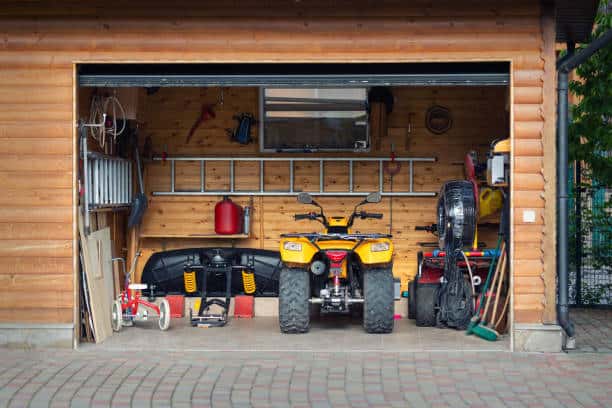 Front view open door ATV quad bike motorcycle parking messy garage building with wooden siding at home driveway backyard and lawn path. House warehouse for tools and equipment.