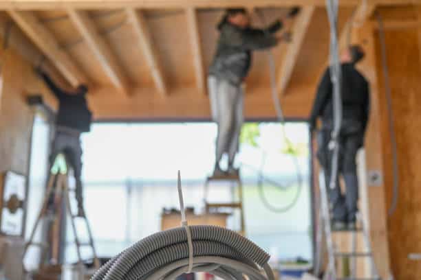 Blurred builders group in room. Tubes and wires hanging from hardwood ceiling. Modern house construction