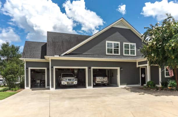 The side view of a large gray craftsman new construction house with a landscaped yard a three car garage and driveway.