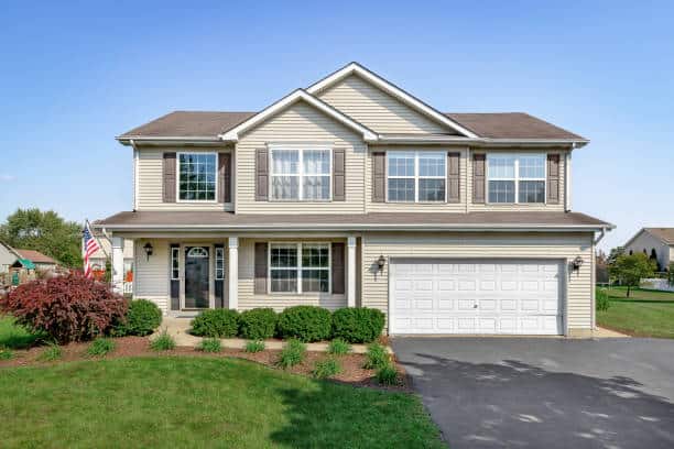 A new suburban house with tan siding, brown window shutters, and a front porch.