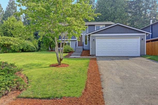 Lovely grey house exterior features grey siding accented with white moldings, attached garage with asphalt driveway and well manicured front yard.